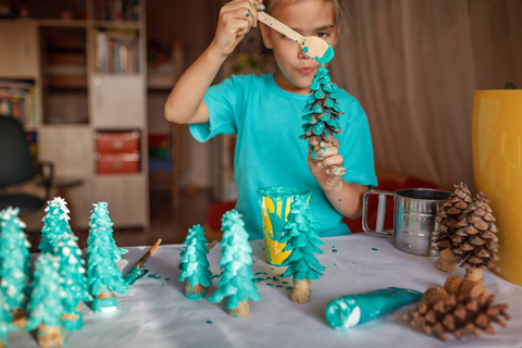A girl painting pinecones into green Christmas trees