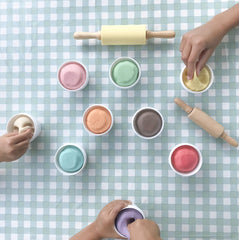children's hands playing with pots of colourful dough on blue gingham table