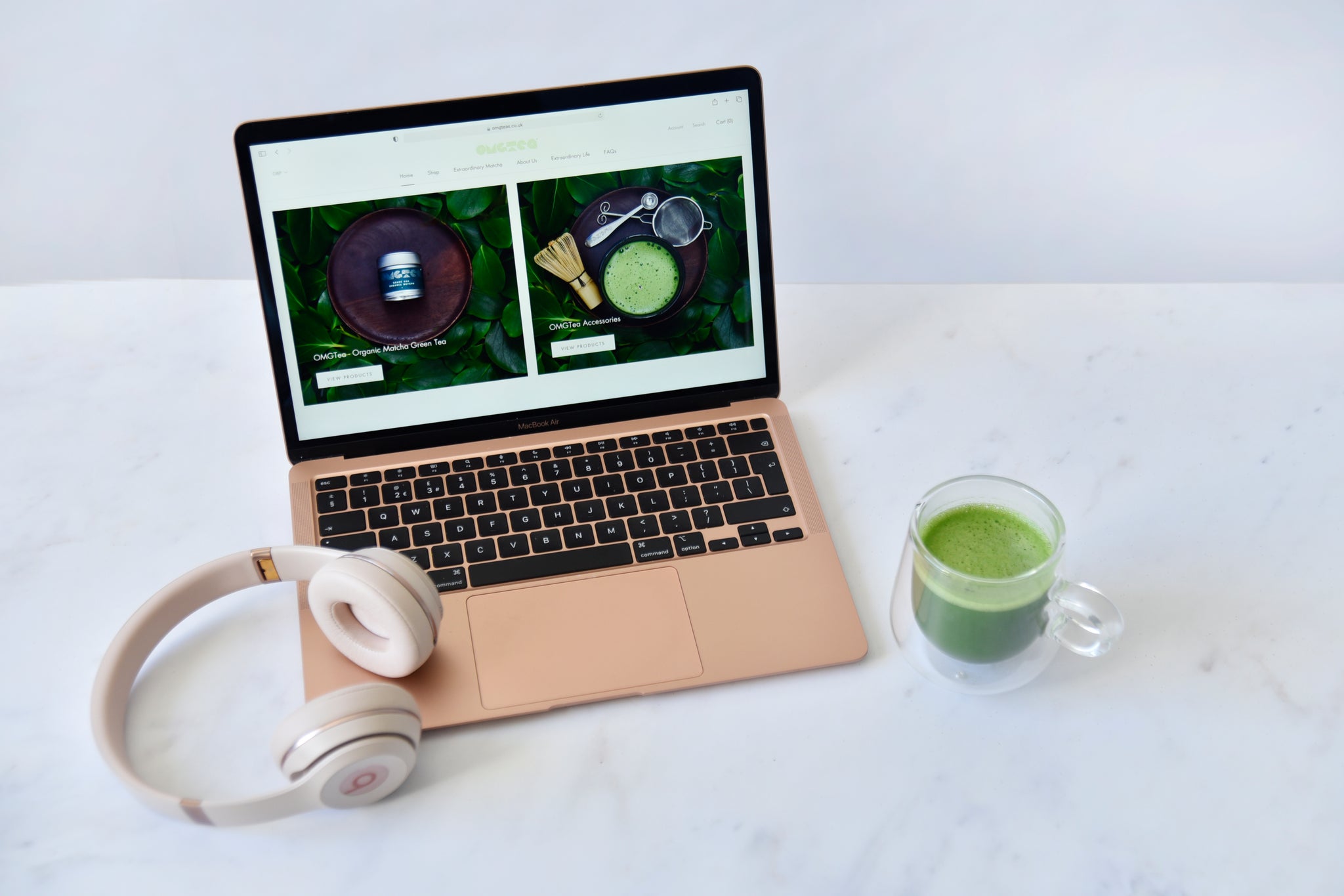 cup of matcha next to macbook air and beats headphones on a marble background