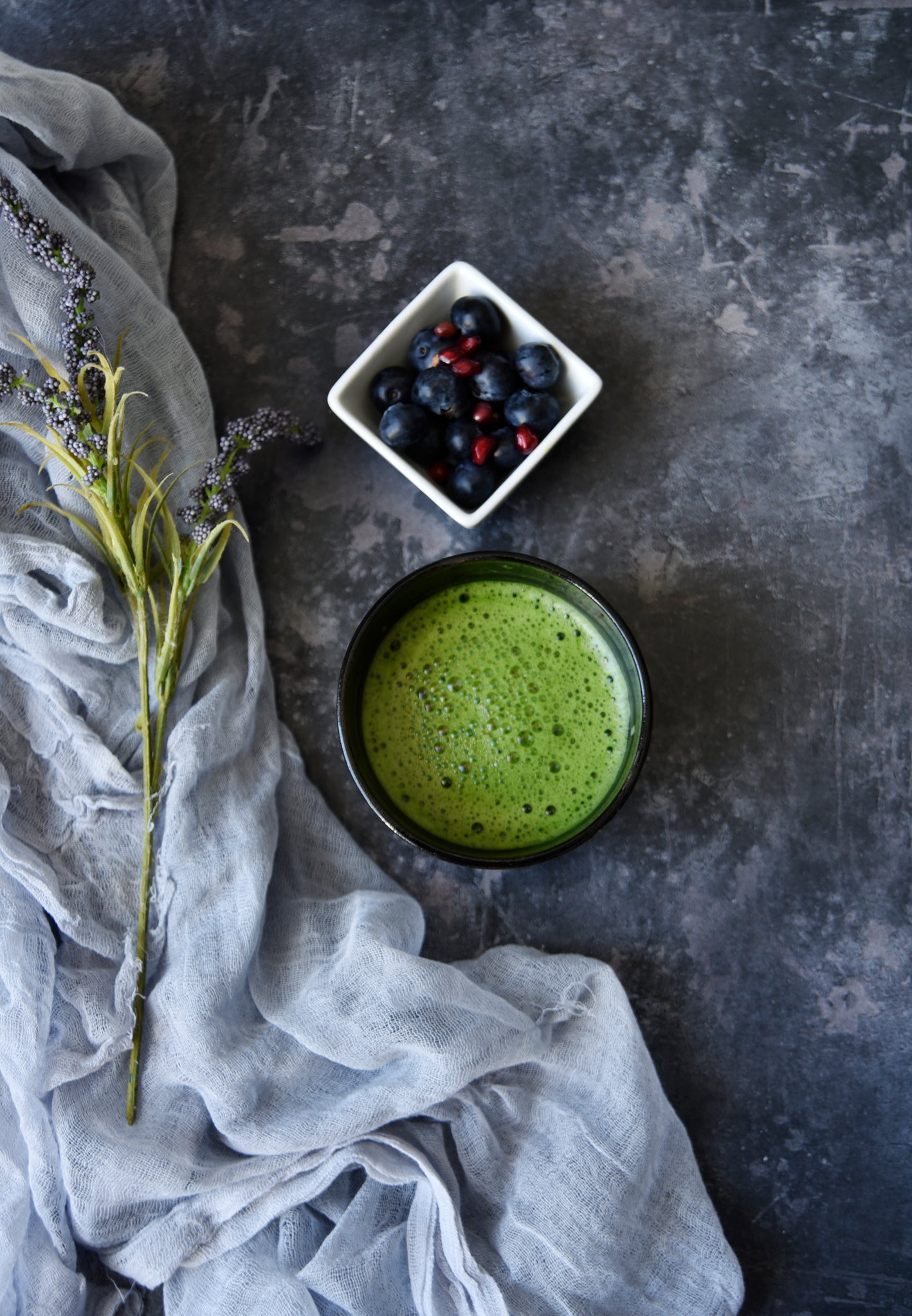 bowl of matcha tea next to bowl with blueberries and pomegranates