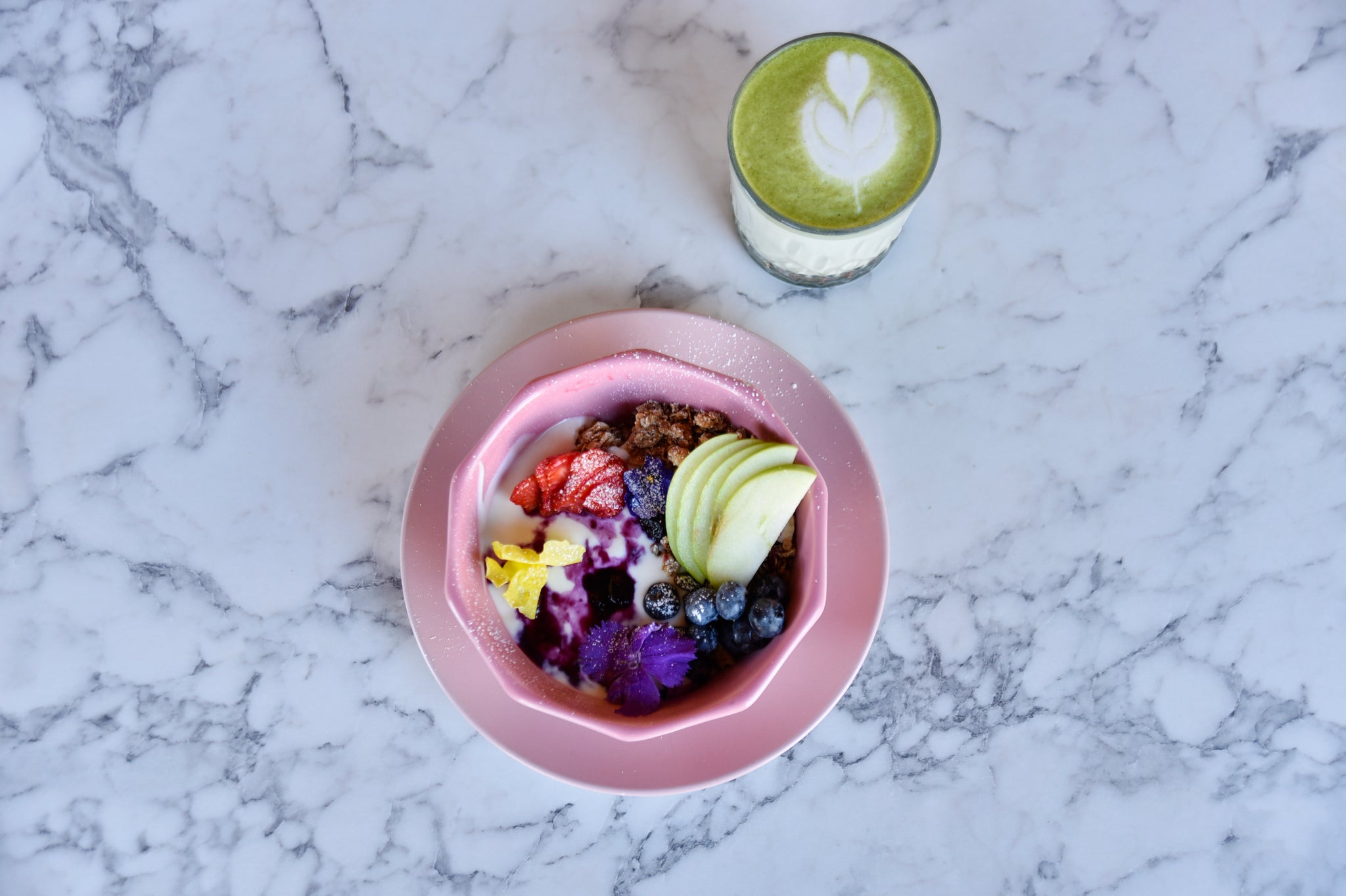 matcha latte and bowl of fruit on marble table