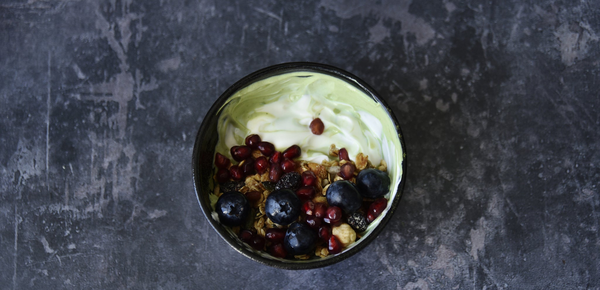 breakfast bowl with matcha on a slate background with a flower next to it