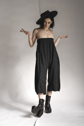 A woman stands in front of a white background wearing a designer hat and an all-black outfit by eigensinnig wien in dark avant-garde style