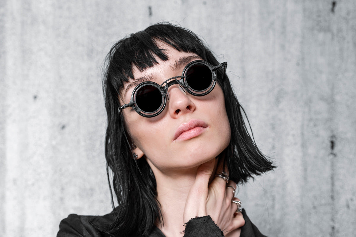 A woman wears designer sunglasses and black clothing in the style of steampunk fashion by eigensinnig wien