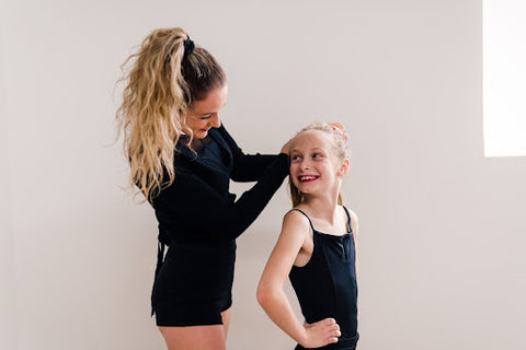 Ballet intrusctor tying a Strongband™️ scrunchie in a child ballerina's hair