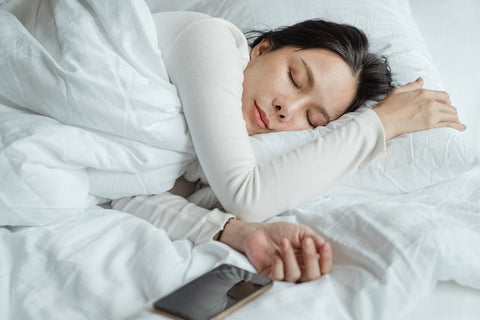 Women sleeps with her head on a pillow and a phone laying next to her. 