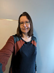Jenn wearing a tunic-length pullover with colourblocking around the shoulders, in navy blue, copper, and teal.