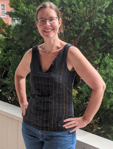 Jenn wearing a v-neck sleeveless top in black with copper metallic stripes. The top is a little tight around the chest and hips.