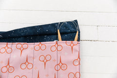 Open needle roll showing a dark blue space print for the outer flap and a pink fabric with scissor print for the inside.