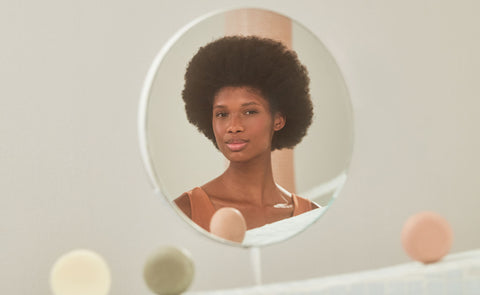 Mulher negra em frente ao espelho com produtos B.O.B no cenário