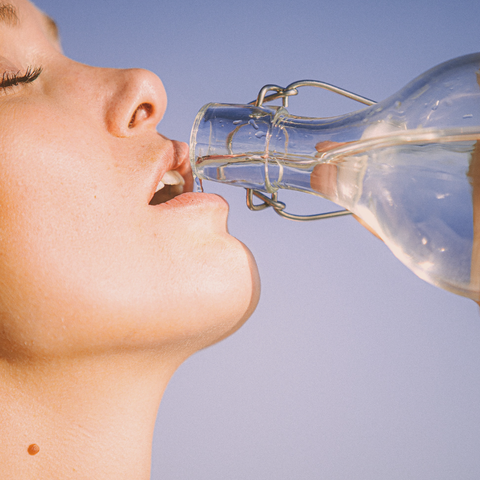 Mulher bebendo água em uma garrafa de vidro