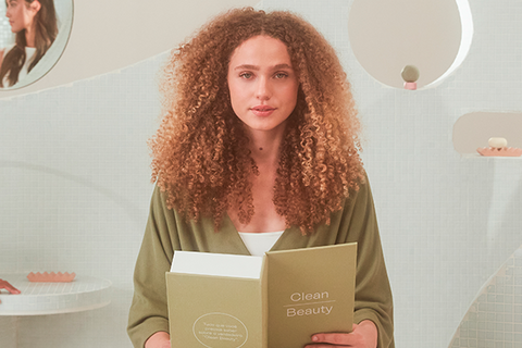Mulher com cabelos cacheados segurando um livro sobre beleza e limpeza