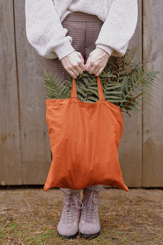moça segurando uma ecobag laranja com plantas dentro