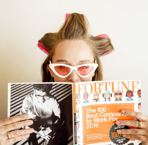 Mulher com bobes no cabelo, óculos com lente vermelha e lendo uma revista
