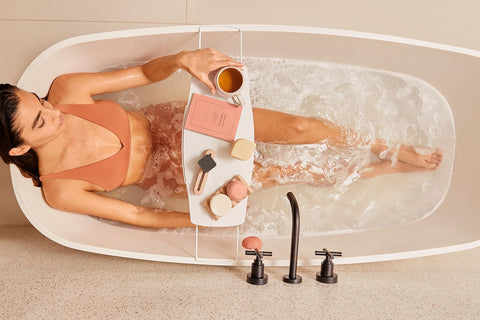 mulher deitada em banheira relaxando com cosméticos em barra