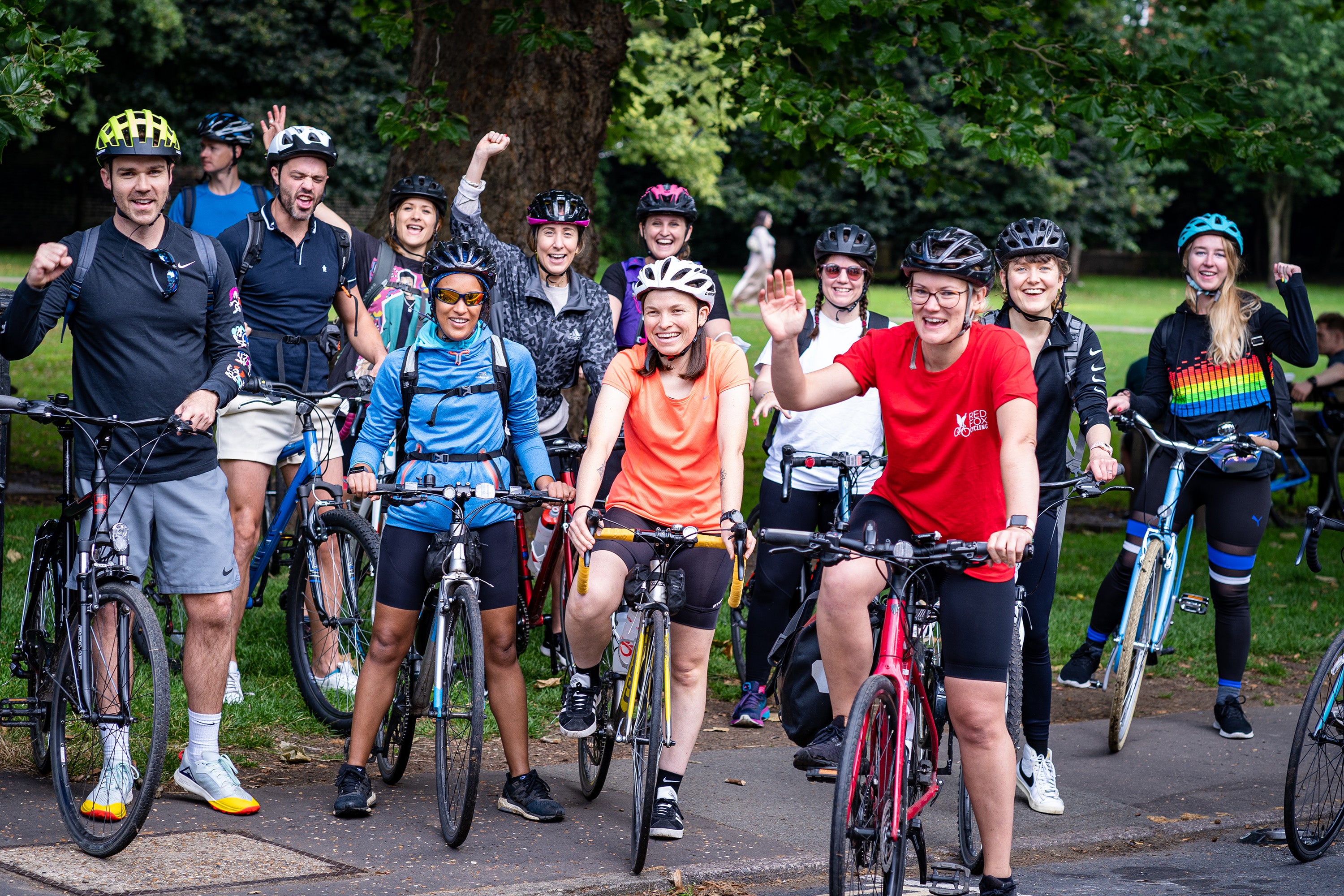 A group of cyclists, stationary on bikes, waving to the camera