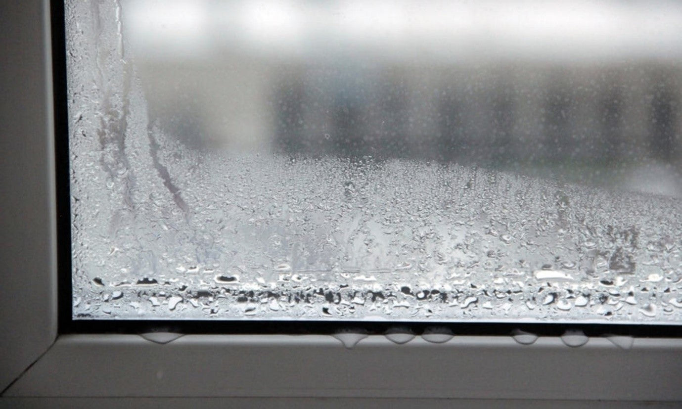 Image of a window with condensation gatgered at the bottom. Full droplets of water are gathered on the window frame.