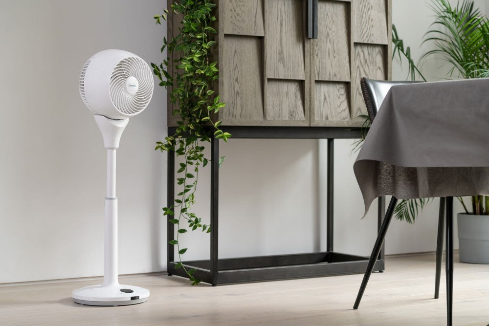Lifestyle image of the Devola 9 inch fan in a modern, stylish dining room. There is a grey wood cabinet with hanging plants and the dinging table has a grey linen tablecloth