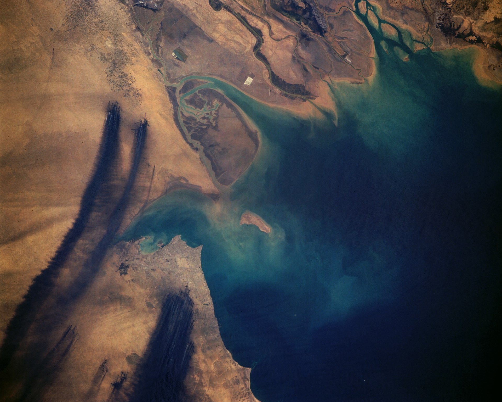 Fotografia aérea capturada do espaço que mostra o fumo negro derivado dos incêndios nos poços de petróleo.