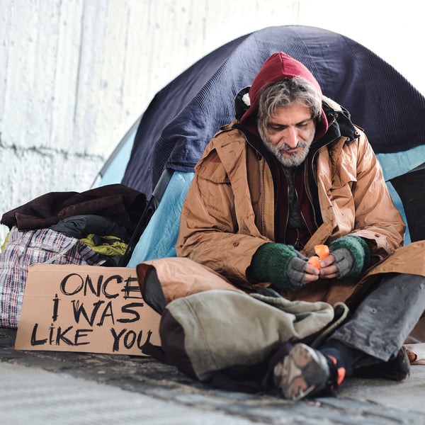 homeless man sitting by a tent peeling an orange
