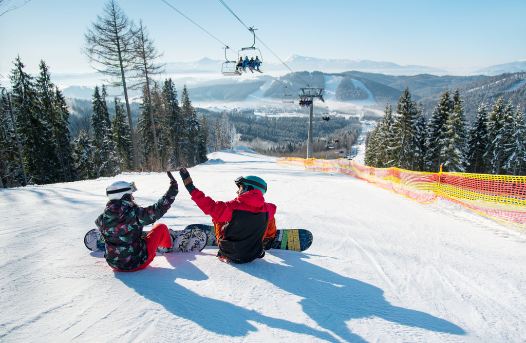 2 snowboarders high fiving on a snowy mountain trail