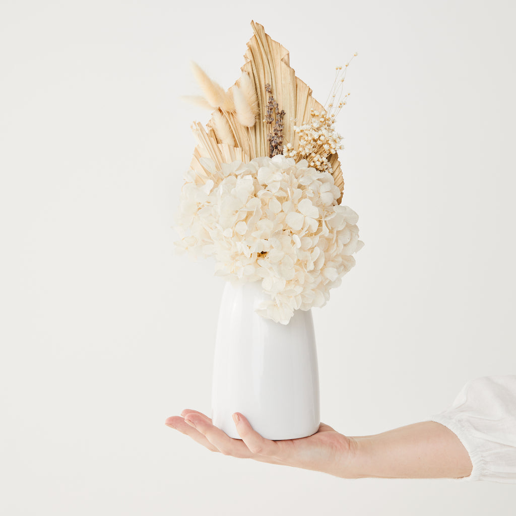 creamy white and natural dried flower arrangement in a white vase