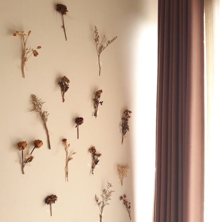 dried flowers taped to a white wall beside a brown curtain, creating a flower wall backdrop