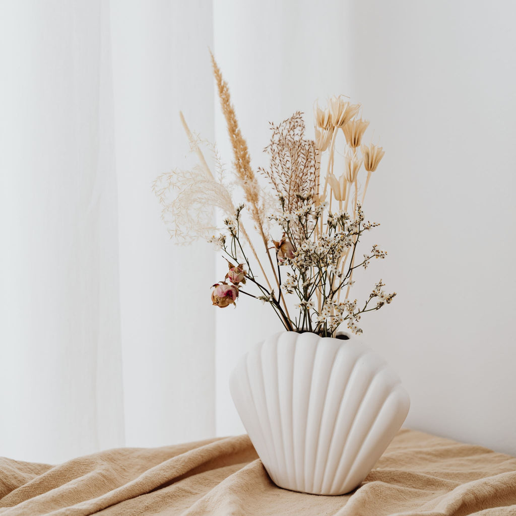 assortment of dried flowers in a white ceramic clamshell-shaped vase