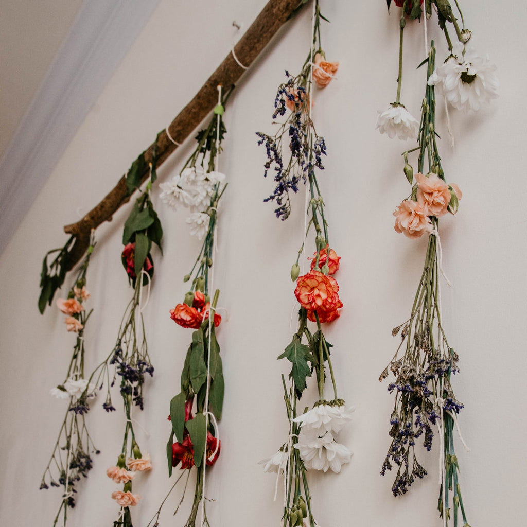 flowers hanging upside down on lengths of twine from a piece of driftwood, to create a dried flower wall hanging