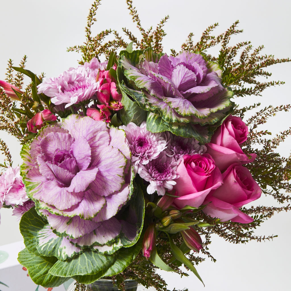 purple and green kale flower in a bouquet among dark pink roses, pink alstroemeria, purple spray chrysanthemums and thryptomene