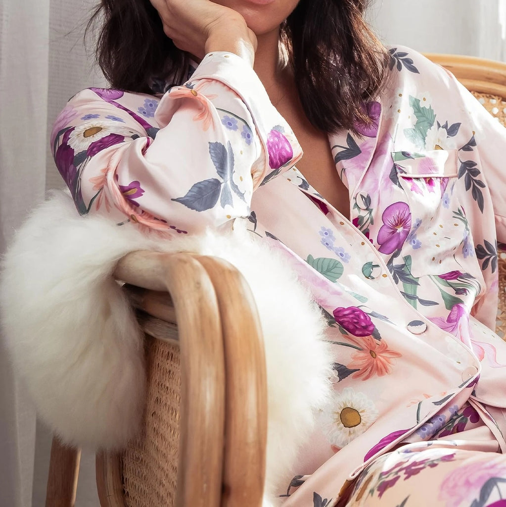 Shop Papinelle sleepwear for Mother's Day. Woman seated in a rattan chair in floral silk Papinelle pyjamas