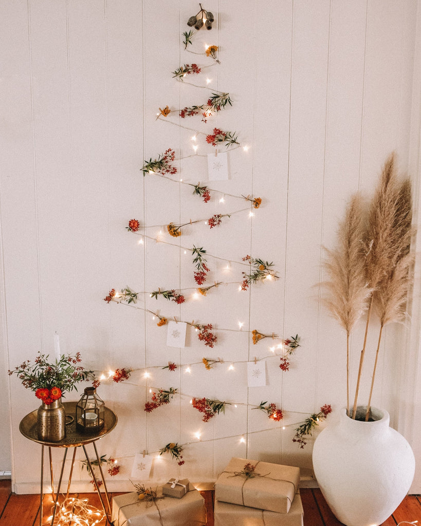 flowers and fairly lights strung up on a wall in a zig-zag formation, creating a christmas tree