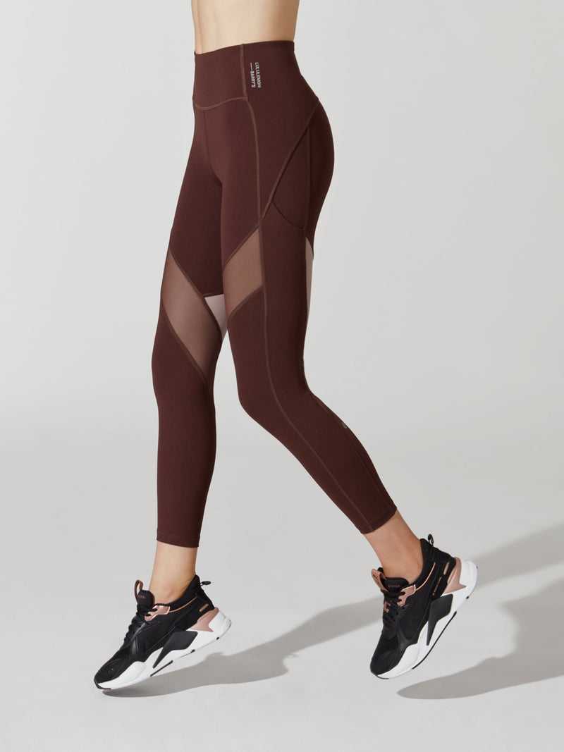 side view of female model in maroon leggings with mesh cutouts on thighs and maroon and pink sneakers