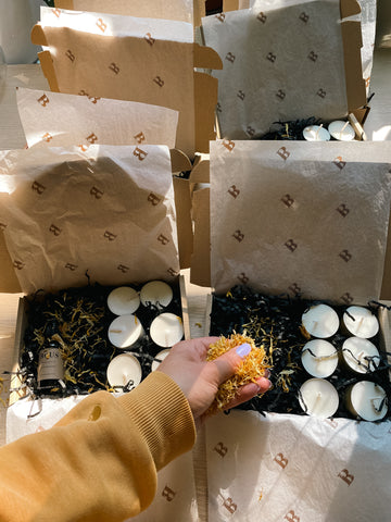 image showing Bous subscription box, this image is showing the making up of the boxes containing Sundrenched essential oil mix in dropper bottle, black crinkle paper filling, branded tissue paper, a sprinkling of marigold flowers and presented in a brown cardboard gift box 