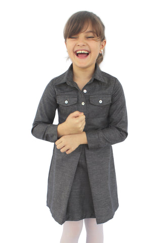 Photo of a young girl wearing our dark grey blue long sleeved shirt dress. It has a pocket on each breast area and a pleat front center of skirt.  It is a short length dress