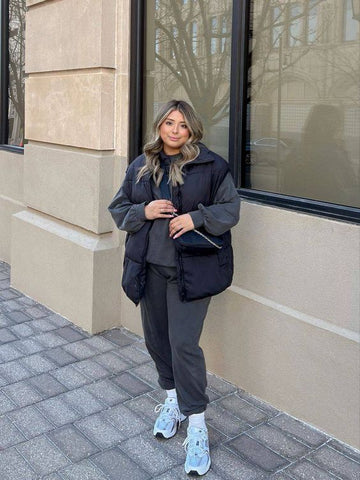 A blonde woman is wearing a sporty outfit including leggings, a hoodie and an oversized black puffy vest. Paired with sneakers.