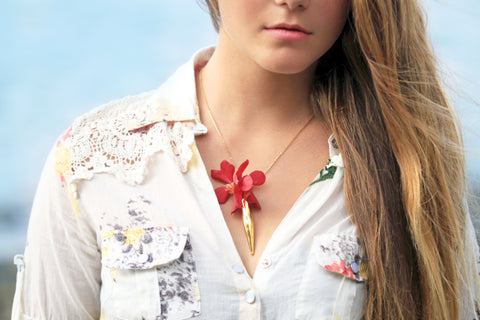 A large gold vase Fleurings necklace that holds water and fresh flowers worn with red vanda orchids. Designed by Samantha Lockwood. Modeled by Alayna McGuiness on the Big Island of Hawaii. 