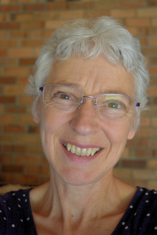 Profile picture of sally ridgway taken in 2024 lady with grey hair and glasses smiling in front of a brick wall