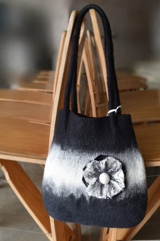 black and white wool felted shoulder bag hanging over a chair with a flower on the front