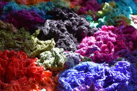 piles of multi coloured silk throwster waste for felting spinning and fibre arts