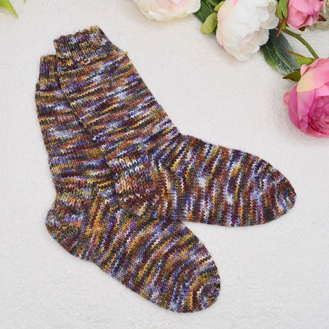 a pair of multicoloured hand knitted socks flat on a white background with silk flowers