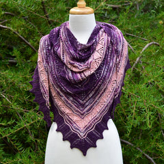 pink and purple lacey knitted shawl using hand dyed yarn on a white mannequin in from of a bush