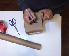 Woman packing and addressing a package to mail. She has tape and scissors nearby for packing supplies.