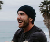 Founder of Windansea Coffee sitting at a beach smiling wearing a beanie