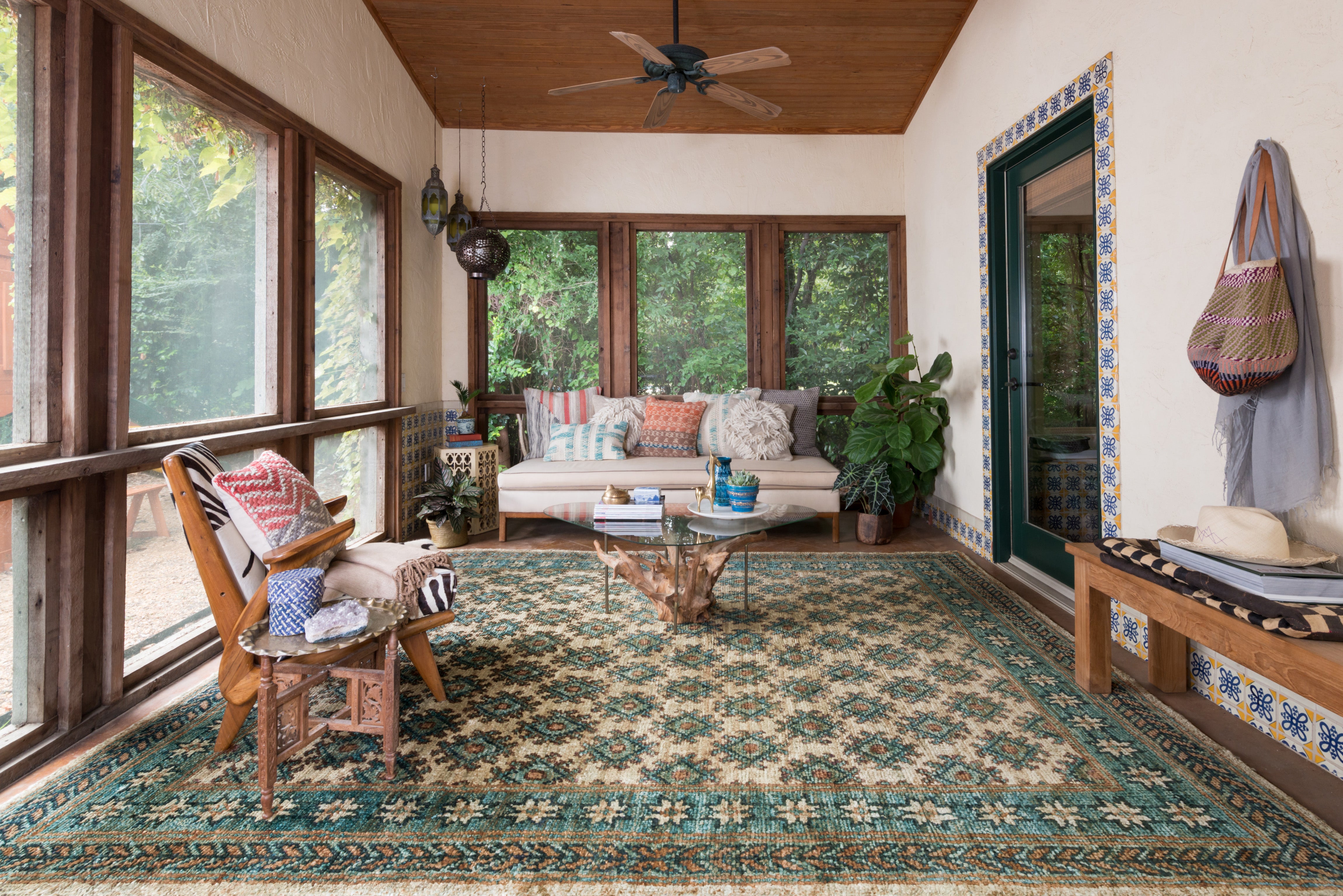 green and ivory area rug on the floor of a rustic looking living room. The ceiling is lined with cedar planks and the furniture is wooden. The coffee table is a reclaimed tree trunk. 