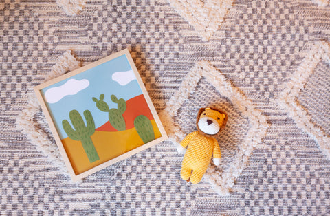 stuffed lion and framed cacti print on top of a grey and white moroccan rug. 