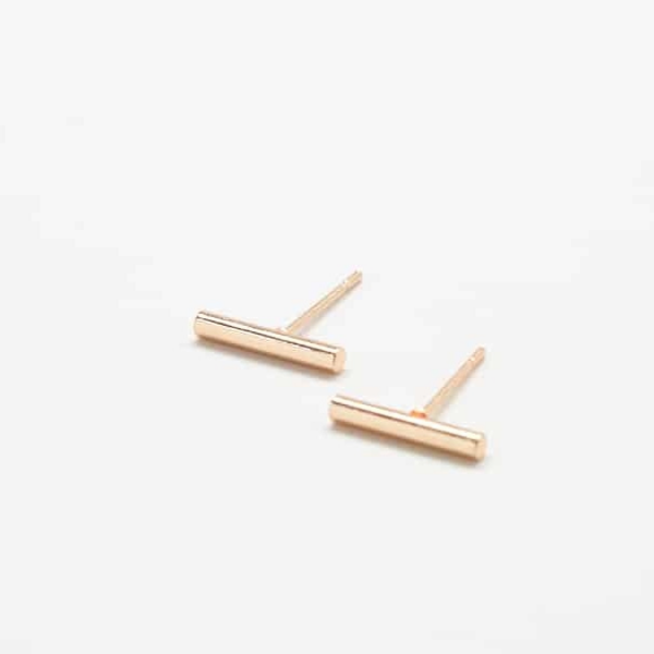 Gold slim bar earrings sitting in front of solid white backdrop