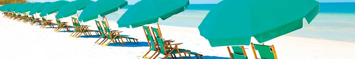 A long row of green beach umbrellas and chairs on a sandy beach with ocean.