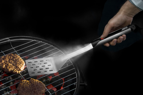 Overhead shot of a hand holding the spatula with a built in flashlight, grilling hamburgers, on a black background