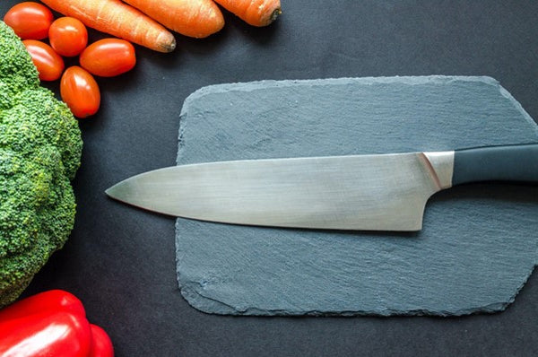 knife on stone cutting board surrounded by vegetables